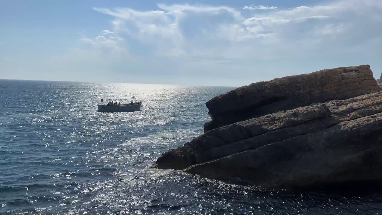 闪闪发光的蓝色银色海浪的岩石海岸线。夏日海面上美丽的云朵。视频素材