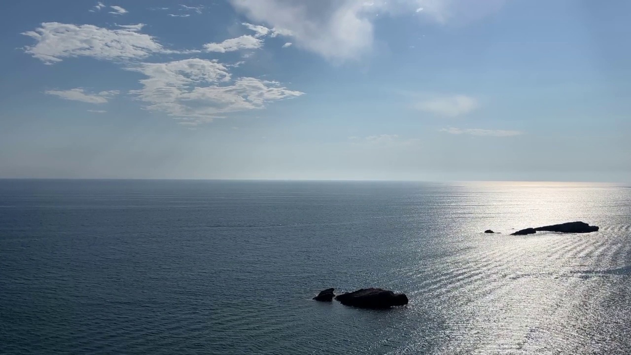 闪闪发光的蓝色银色海浪的岩石海岸线。夏日海面上美丽的云朵。视频素材