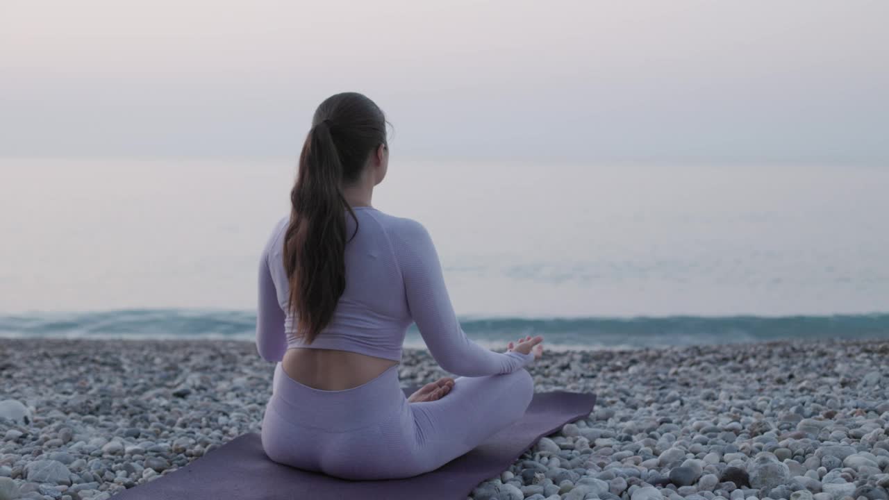 健康年轻女子练习瑜伽莲花姿势附近平静的大海在日出，心理健康的概念视频素材