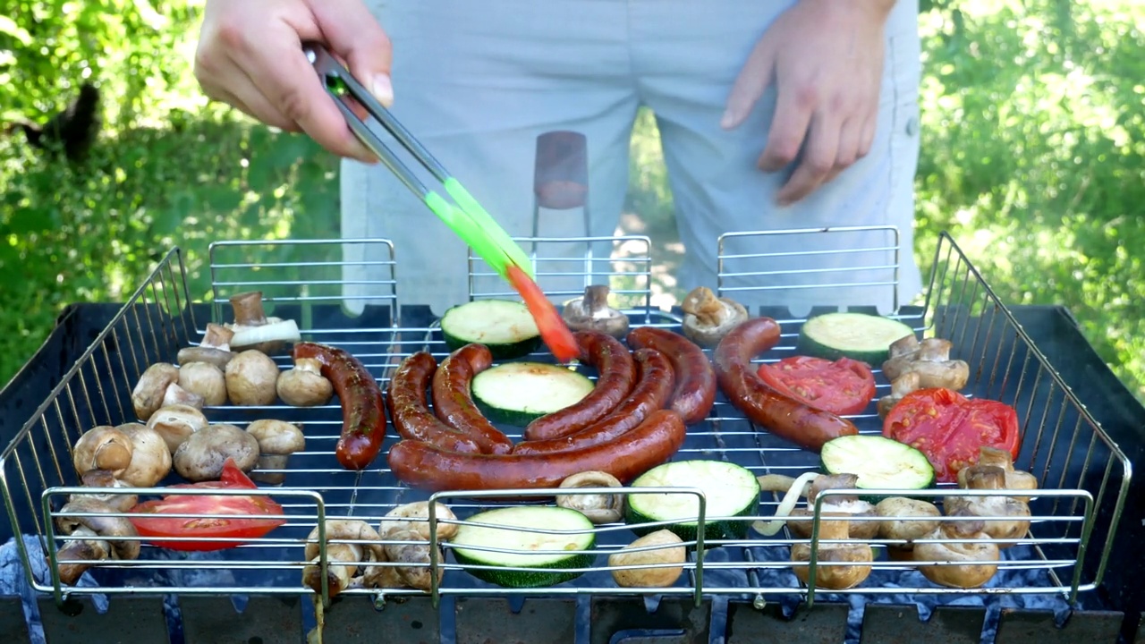 在烤架上烤。室外烤架上的油炸香肠和蔬菜。B-B-Q。油炸食品是在木炭烤架上油炸和烟熏的。原来是一个烤炉，里面有美味的香肠，蔬菜，香菇。野餐和露营街头食物视频素材