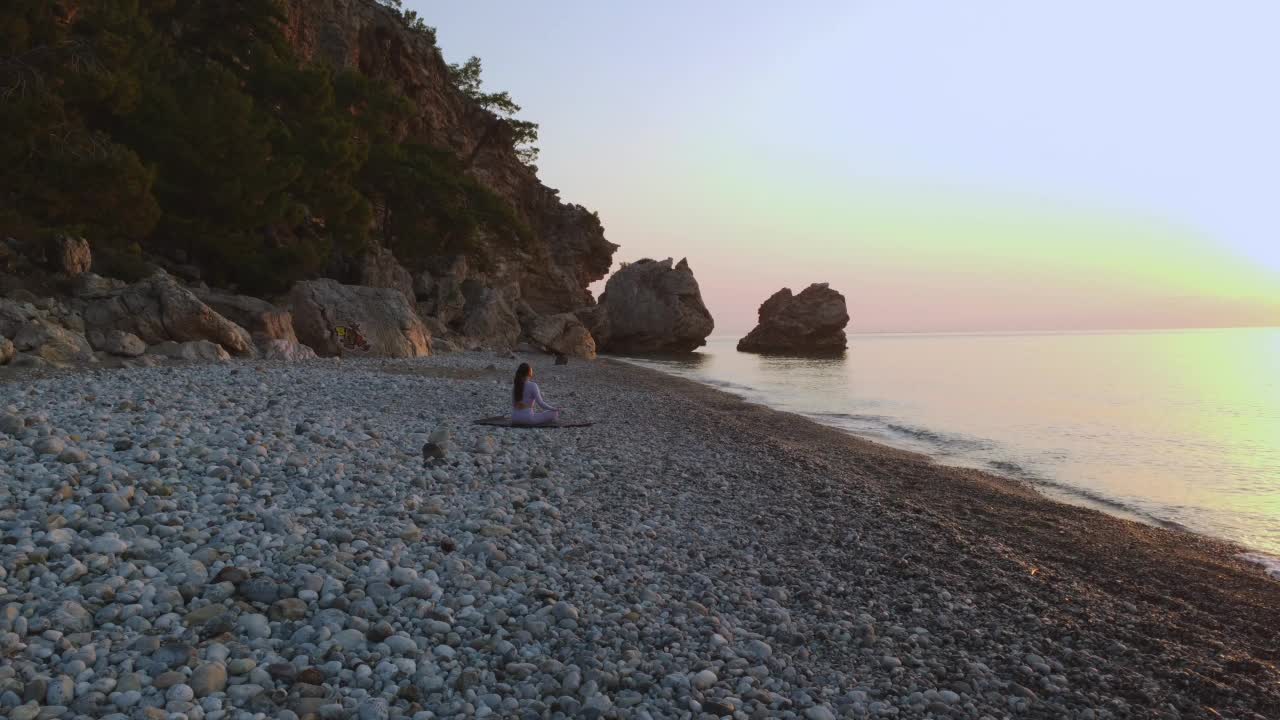 健康年轻女子练习瑜伽莲花姿势附近平静的大海在日出，心理健康的概念视频素材