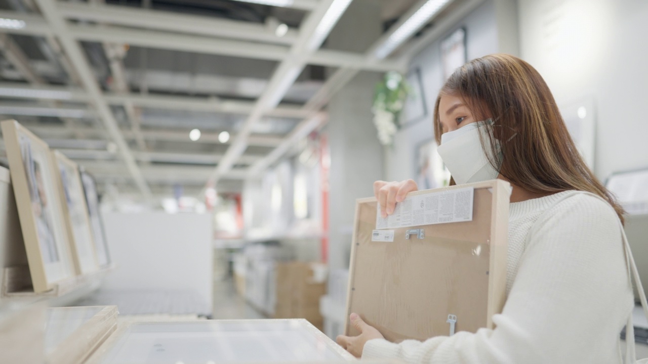 年轻女子在家具店购物，疫情期间买家戴着防护口罩购物，新常态零售商店。视频下载