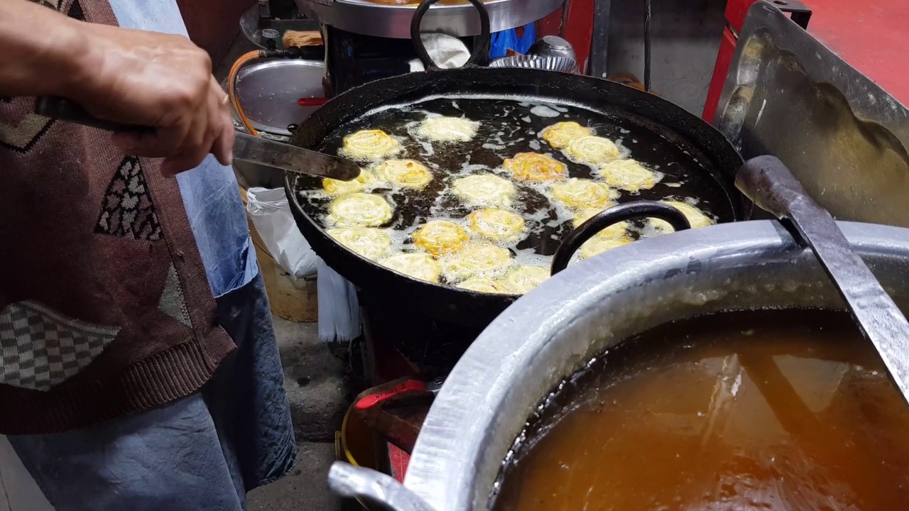 在街市小摊上，一名卖甜食的小贩正在用平底锅烹饪和翻转加勒比(甜)。视频素材