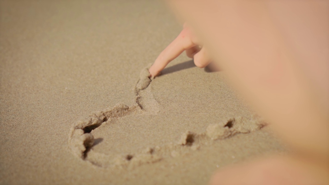 女孩手绘的心在海滩上近距离和它洗出的海浪视频素材