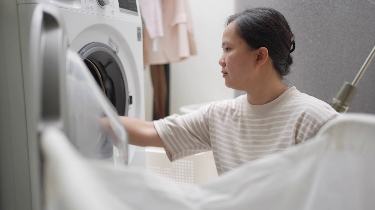 一名年轻女子正在家里把衣服装进洗衣机。妻子做家务视频素材