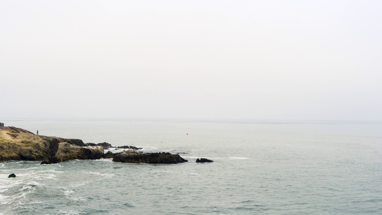 空中扫荡着暴风雨般的海岸线，波涛汹涌，灰色的天空，人们走在一个点上——加州马里布视频素材