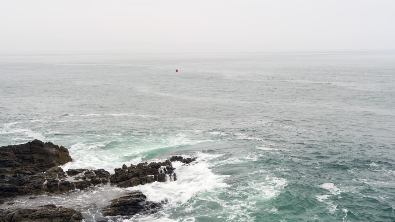 空中倒转，一个孤独的女人站在岩石和暴风雨的海岸线上，撞击的海浪和一群海鸟附近-加州马里布视频素材