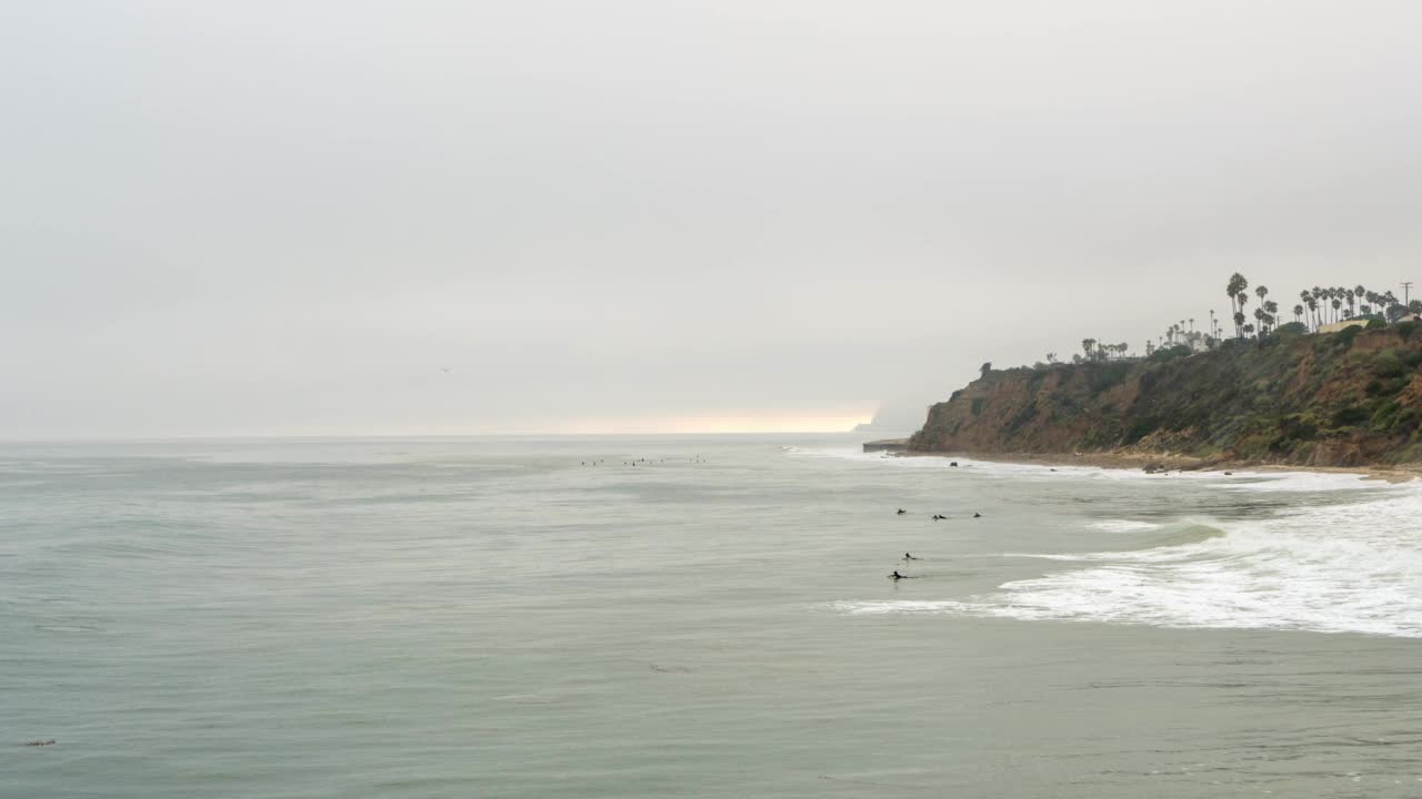 与冲浪者，撞击的海浪，和灰色的天空空中摇一个暴风雨的海岸线-马里布，加州视频素材