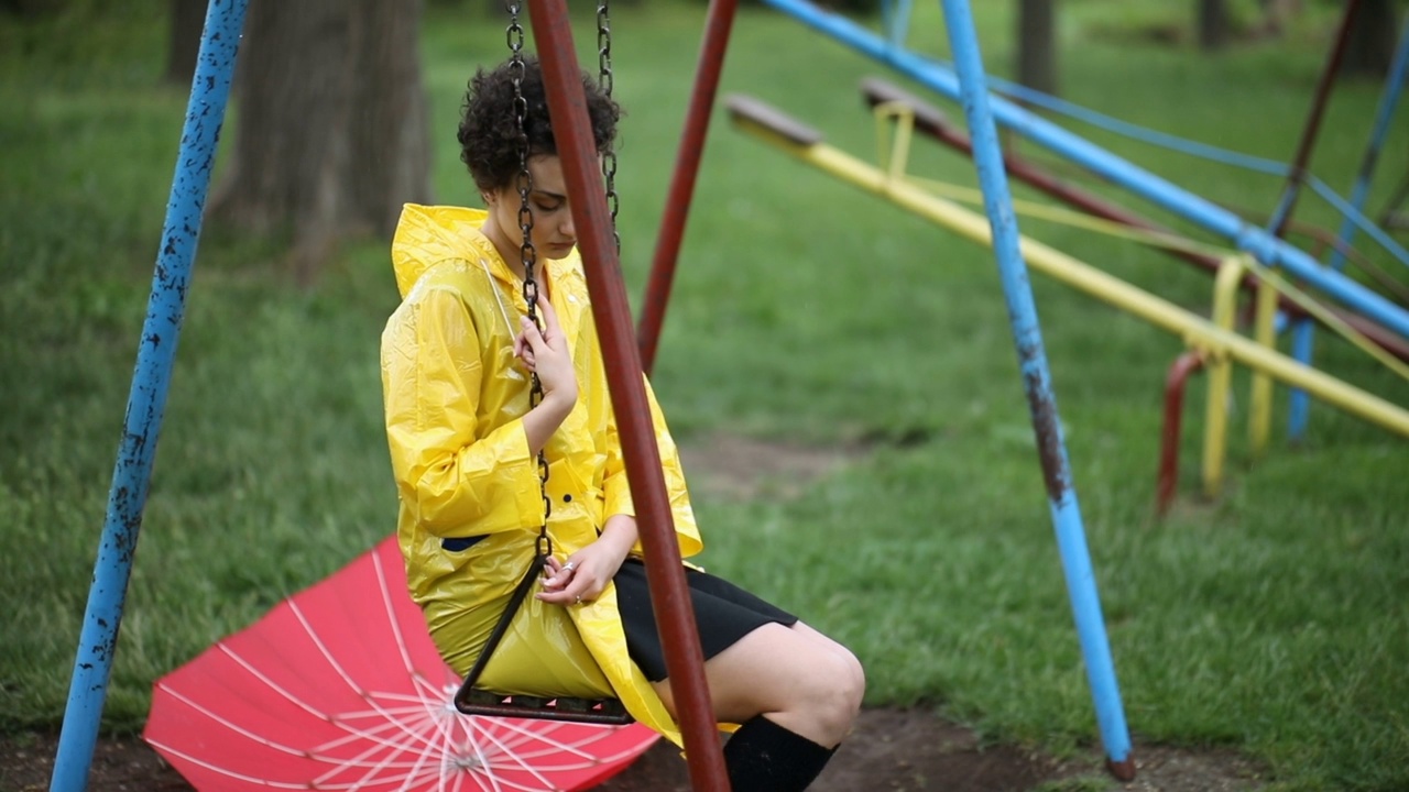 一个悲伤的年轻女人在雨天荡秋千视频素材