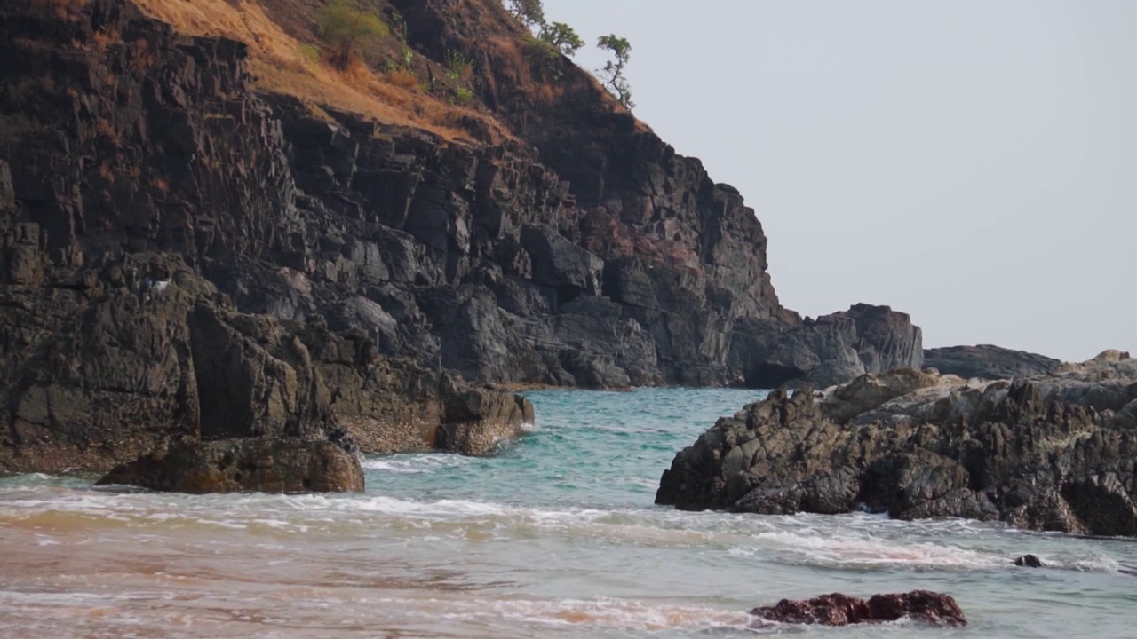 从印度果阿的Kakolem海滩看到，海浪撞击在海上的岩石。海浪拍打着大海中央的岩石。自然放松的背景。在蓝色的海水中间的岩石。视频素材