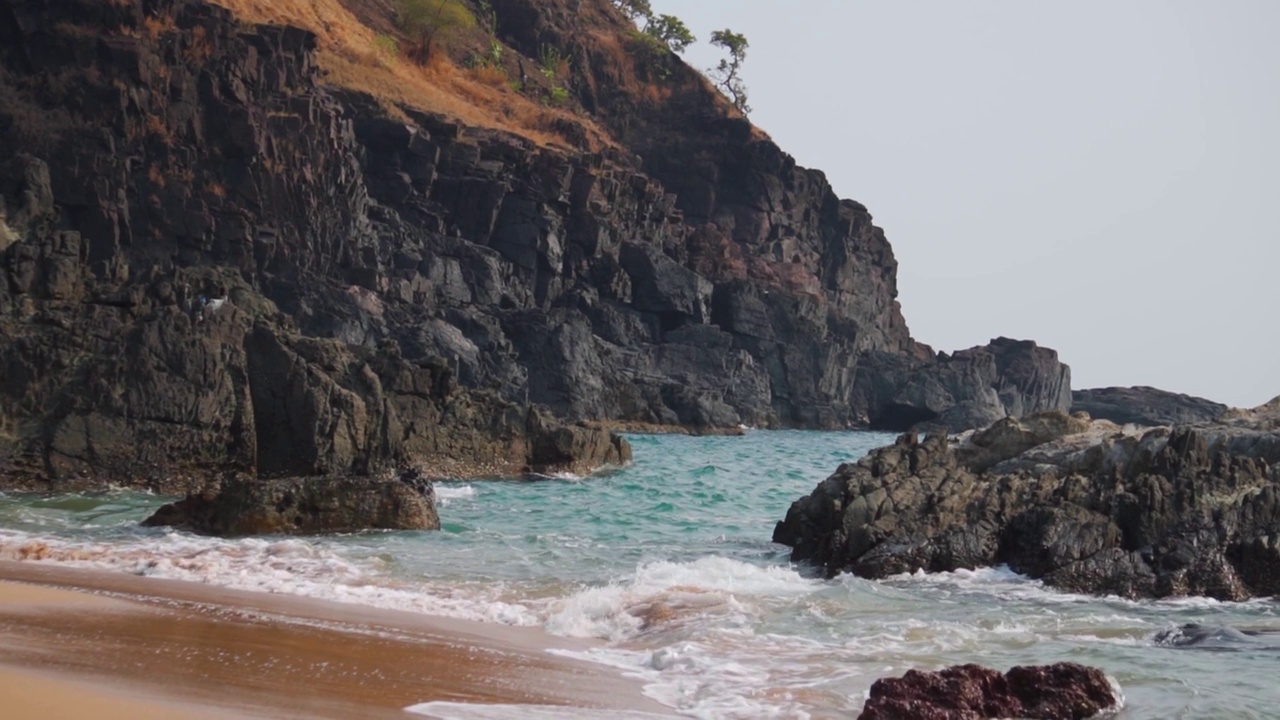 从印度果阿的Kakolem海滩看到，海浪撞击在海上的岩石。海浪拍打着大海中央的岩石。自然放松的背景。在蓝色的海水中间的岩石。视频素材