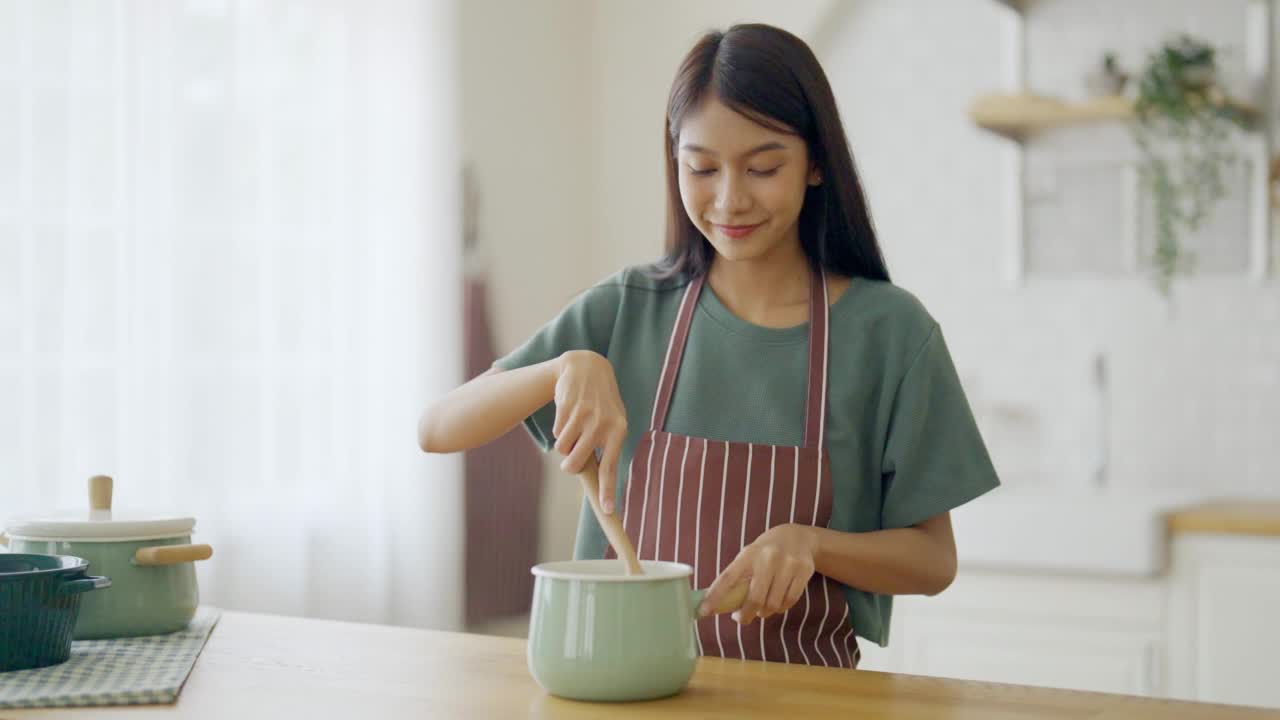 年轻美丽的亚洲女人在家里厨房做饭视频素材