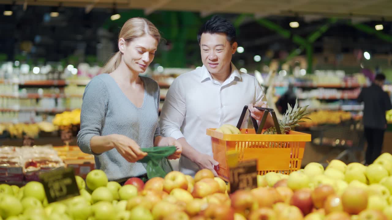 幸福的混合种族亚洲夫妇家庭男人和女人在杂货店和超市选择水果或蔬菜。每日一起购物视频素材