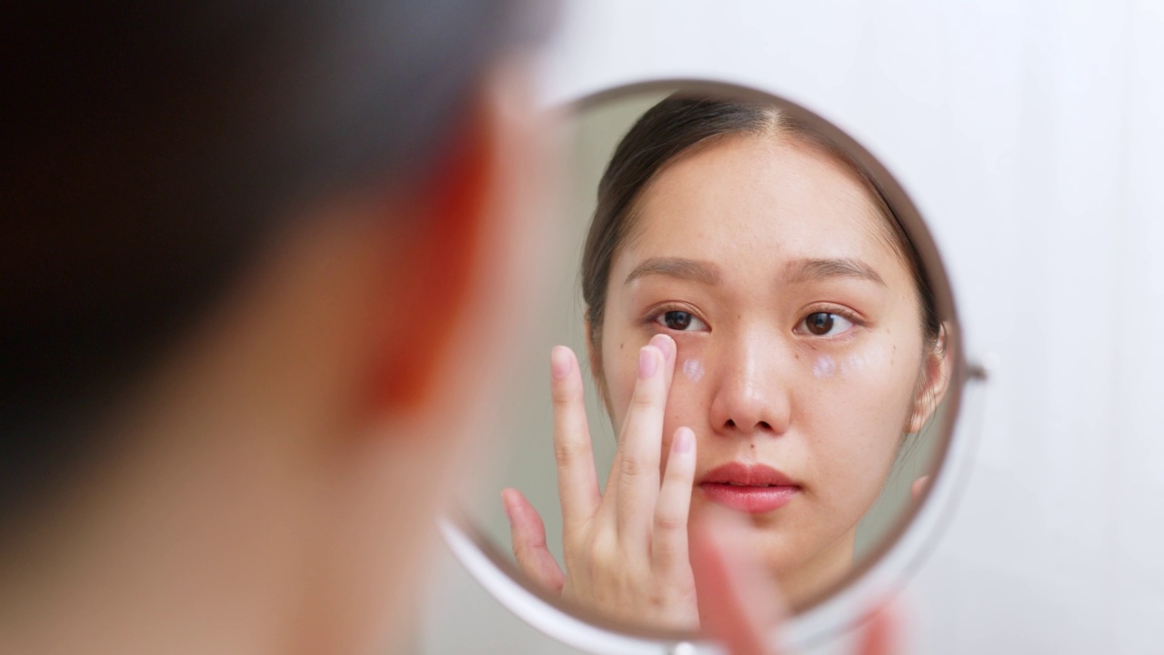 年轻的亚洲美女应用眼霜在健康的面部皮肤，亚洲美容皮肤的概念视频素材