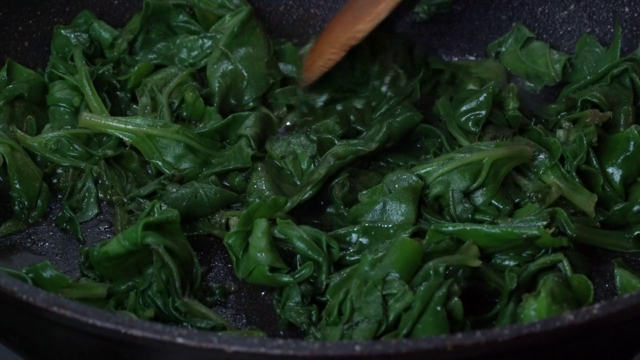 用煎锅煮菠菜的特写。新鲜的菠菜被扔进煎锅里视频下载