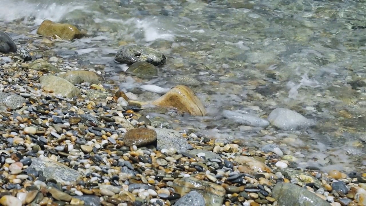 海浪和卵石海岸。多石的海滩卵石在岸边和翻滚的海浪溅起水花。特写镜头视频素材