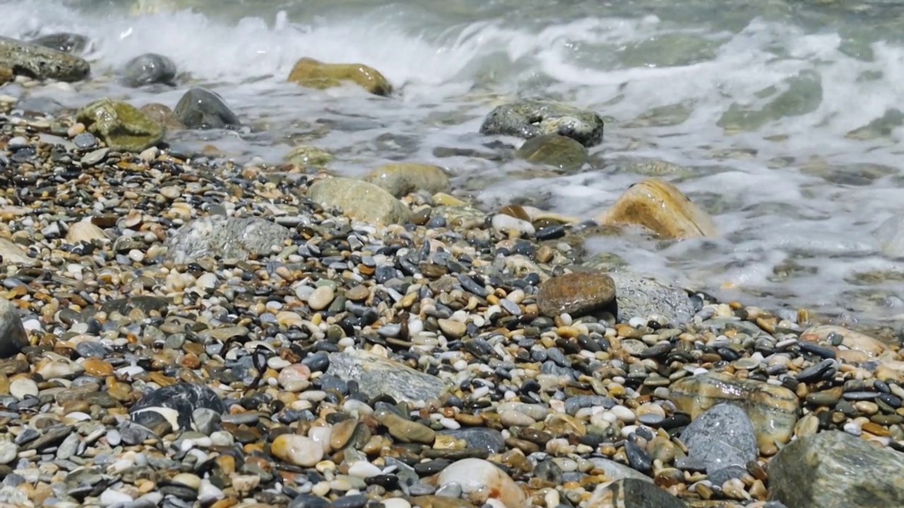 海浪和卵石海岸。多石的海滩卵石在岸边和翻滚的海浪溅起水花。特写镜头视频素材