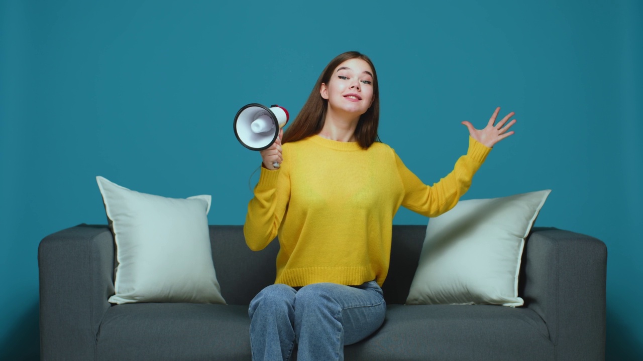 现代年轻女孩用扩音器宣布大减价。女警告用扩音器，坐在沙发上视频素材