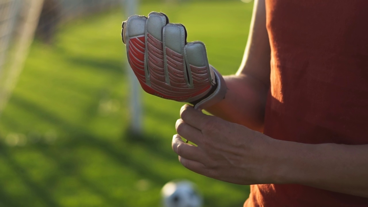 年轻的足球守门员戴着手套站在足球场。视频素材