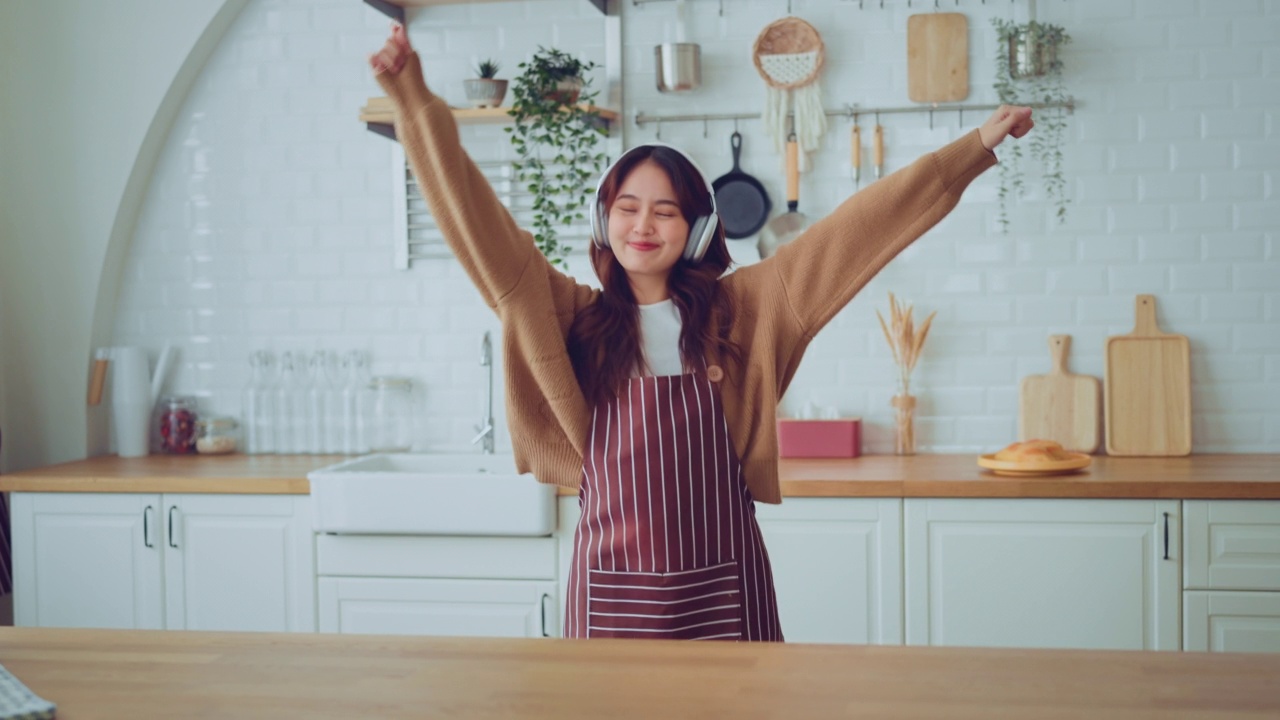 慢动作的快乐年轻的亚洲女人跳舞与耳机在家里有乐趣放松与有趣的舞蹈动作享受自由的周末早上。视频素材