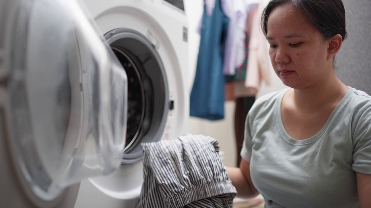 一名年轻女子正在家里把衣服装进洗衣机。妻子做家务视频素材