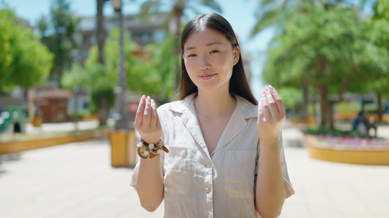 中国女子在公园微笑着自信地做着花钱的手势视频素材