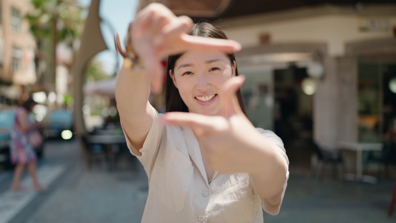 中国女人微笑着自信地在街上用手做拍照的姿势视频素材