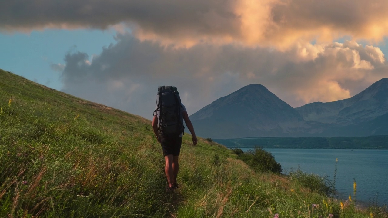 背着双肩包沿着山区海岸徒步旅行的男人。慢动作视频素材