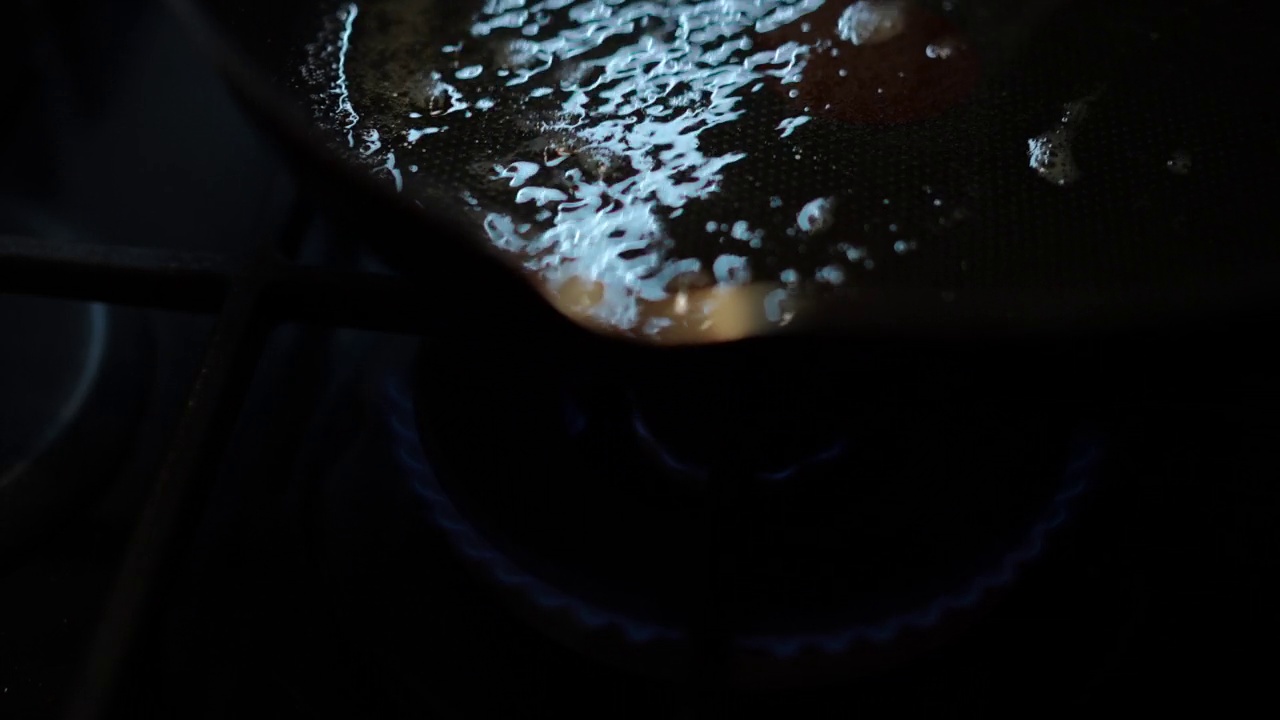 特写植物油在煎锅沸腾作为未知的人摇晃烹饪锅。无法辨认的男人或女人在厨房烹饪室内特写。视频素材