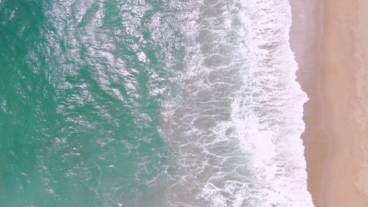 俯视碧蓝海水，波浪飞溅，海岸线艳阳高照。视频素材