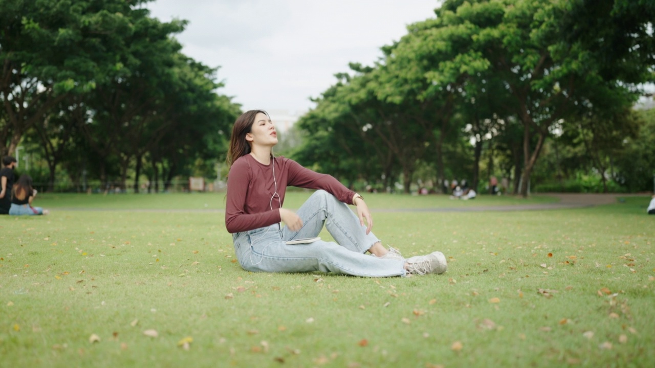 美丽的女孩在绿色公园里戴着耳机用智能手机听音乐视频素材