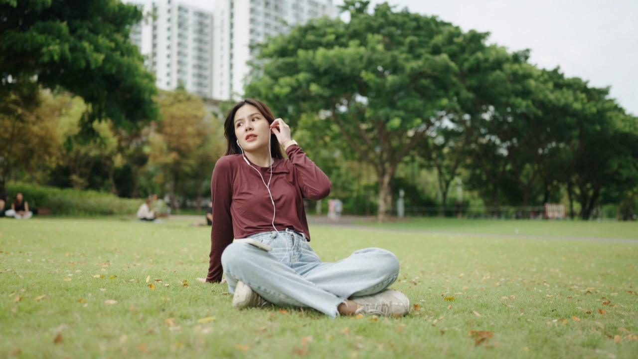 美丽的女孩在绿色公园里戴着耳机用智能手机听音乐视频素材