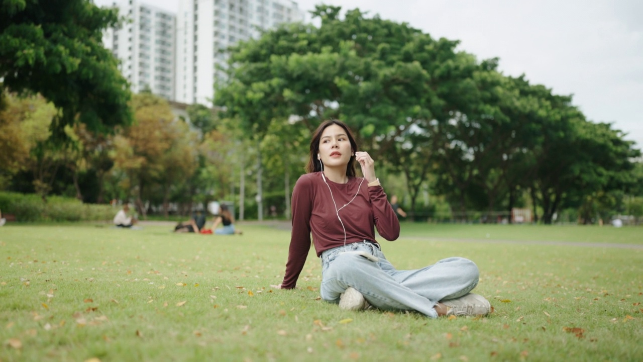 美丽的女孩在绿色公园里戴着耳机用智能手机听音乐视频素材