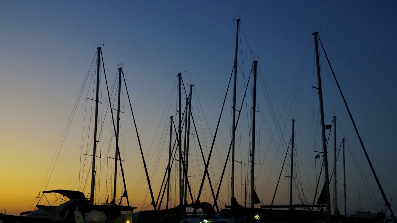 游艇桅杆映衬着夜空。美丽的背景，港口的夕阳。游艇和桅杆在波浪中摇摆。视频素材