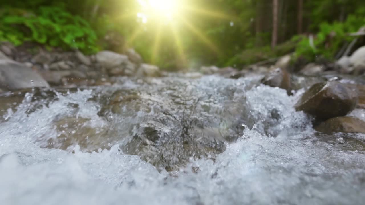 森林里湍急的山河。相机沿着水面和石头的表面移动，夕阳和绿色植物在背景中。慢动作超高清镜头视频素材