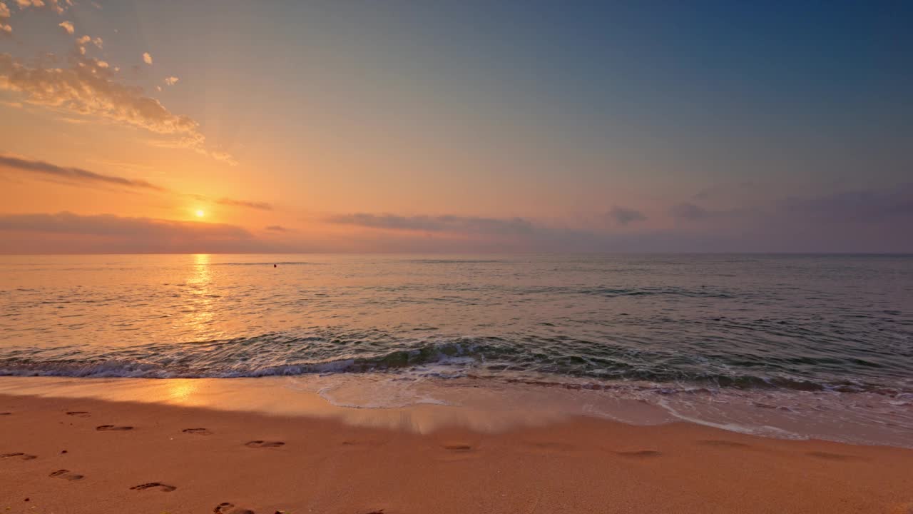 海洋沙滩日出，彩色云和太阳光线在海浪上，4K视频景观。沙滩上的脚印。视频素材