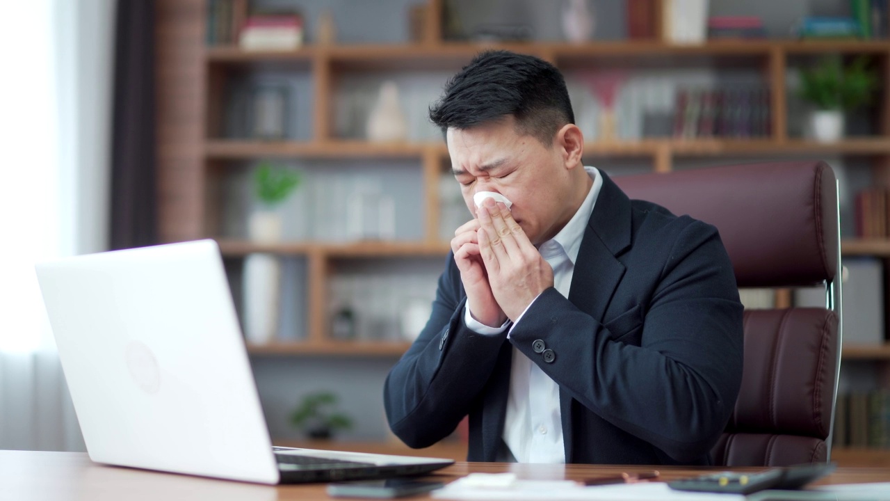 成熟的商人亚洲男性工人患有头痛过敏，打喷嚏流鼻涕。员工在办公室工作时咳嗽感冒或流感。室内。视频素材