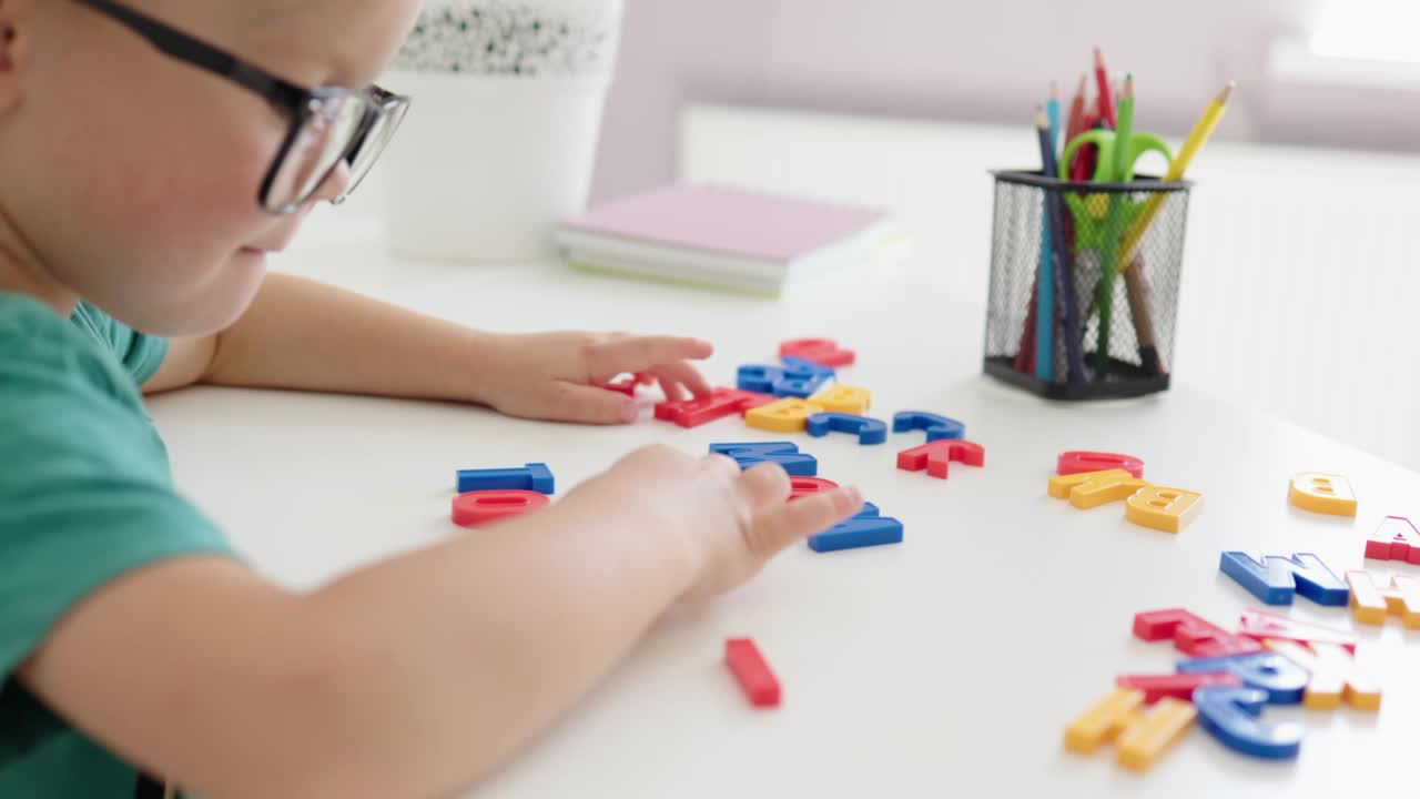 聪明的小男孩戴着眼镜坐在桌子旁，把ABC字母放进单词玩具里视频素材