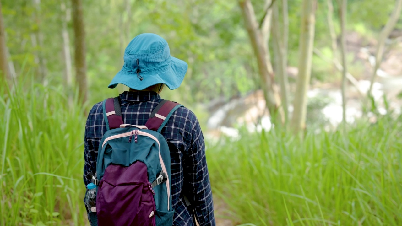 4K，一个喜欢在森林里旅行和徒步旅行的亚洲女人独自走在通往瀑布的森林里。周末从工作中放松一下。视频素材