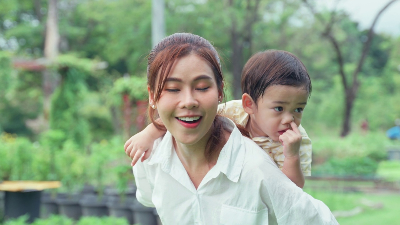 妈妈背着小儿子，带着可爱的小儿子出去玩。视频素材