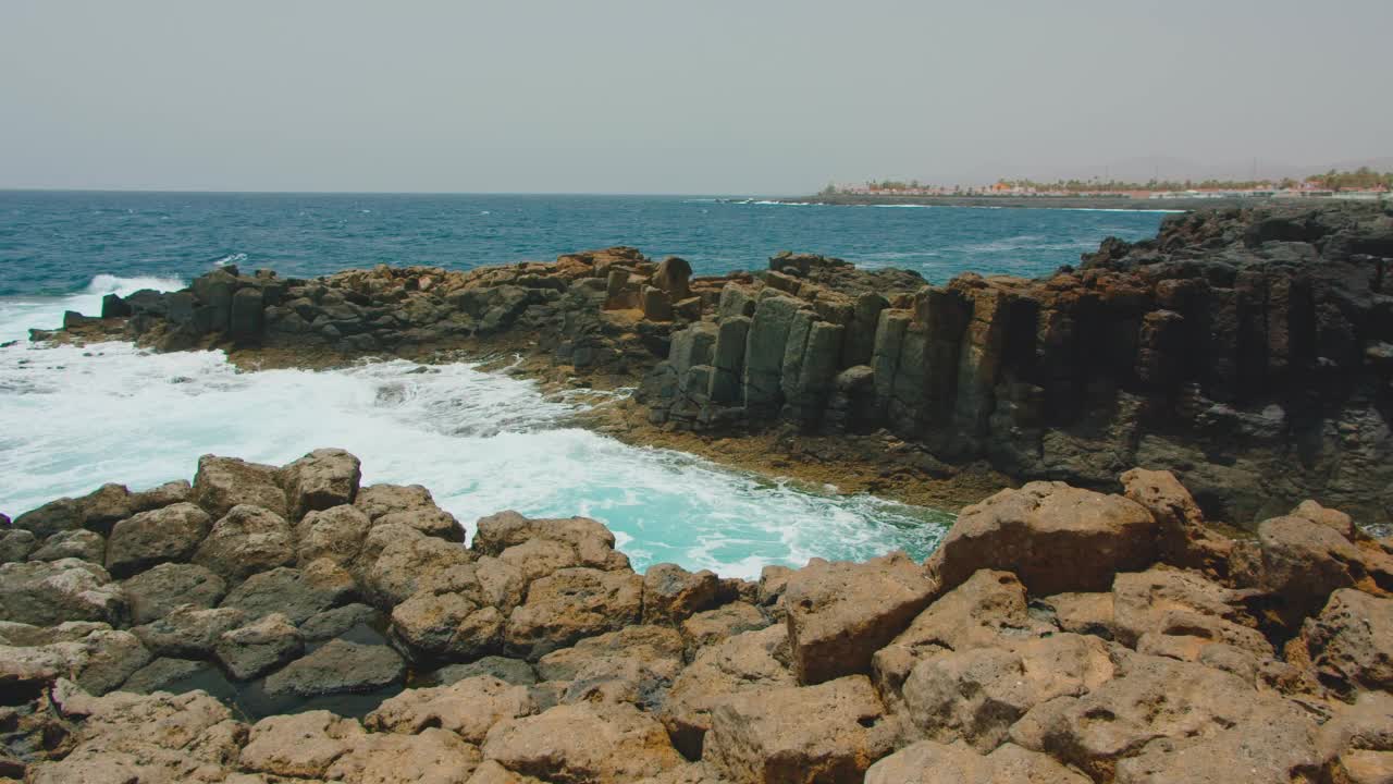 海浪冲击着空荡荡的岩石黑色海滩。蓝色海水打破海岸线。近距离拍摄的火山石，水花飞溅的海岸线。视频素材