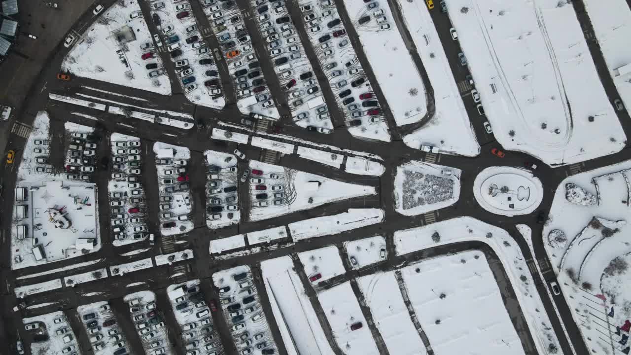 冬季繁忙的购物中心停车场，停车场被雪覆盖，冬季下雪天现代商场或购物中心附近的大型汽车停车场鸟瞰图。一排排车辆的停车场视频素材