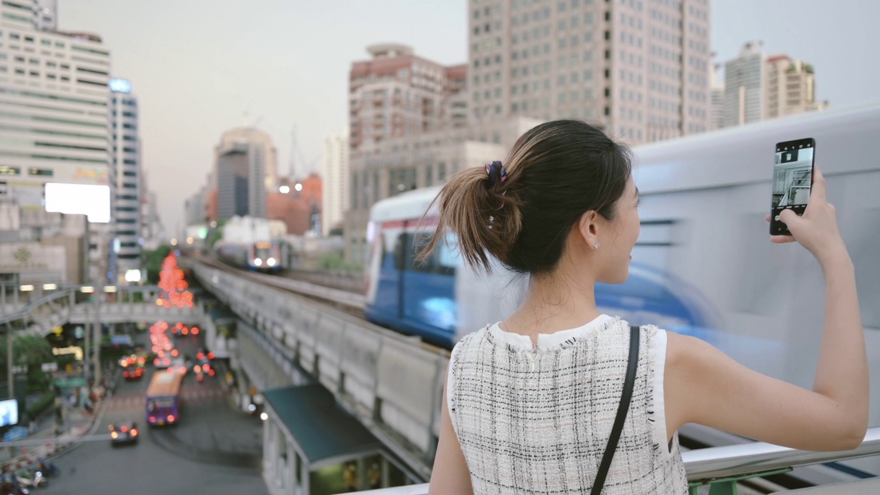 在泰国曼谷，在BTS Skytrain轨道地铁城市生活和交通等火车的亚洲中年女性商业女性办公室享受周五通过智能手机使用社交网络连接视频素材