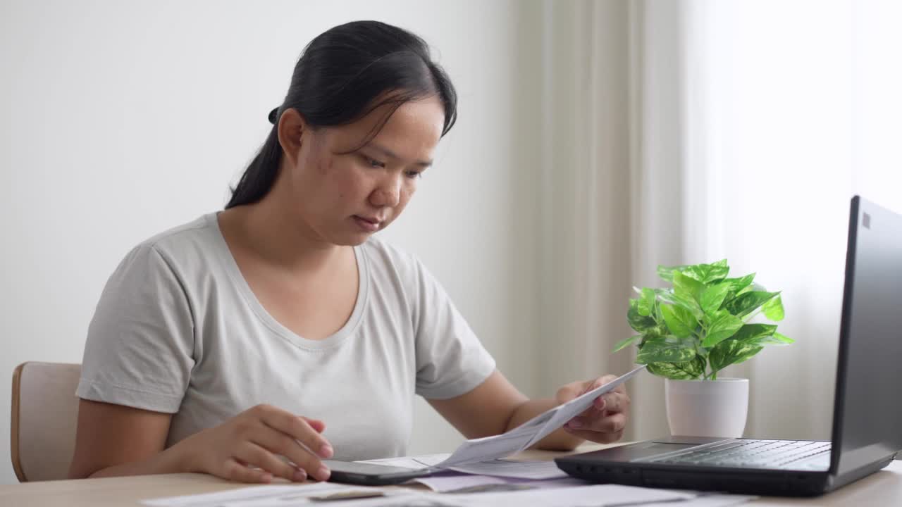 压力大的亚洲年轻女性管理财务和信用卡账单，在家里用手机计算家庭财务债务。一个做开支计划的妻子视频素材