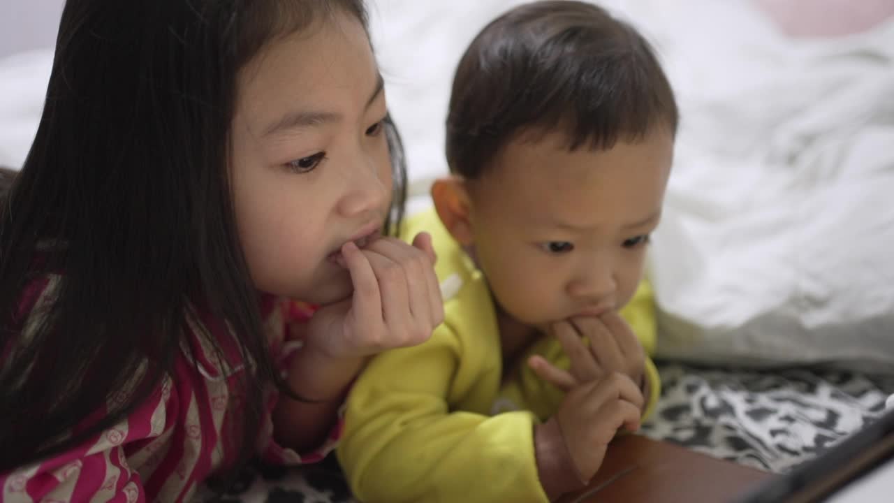 妹妹和弟弟在睡觉前看平板电脑。关注这个女孩视频素材