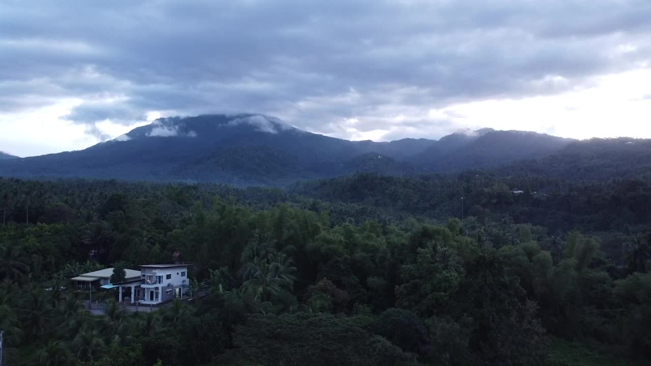 无人机在丛林上空飞行，丛林中有一座带有种植园的豪宅。热带岛屿有高山和郁郁葱葱的动植物。无人机在岛上的棕榈树上空飞行。视频素材