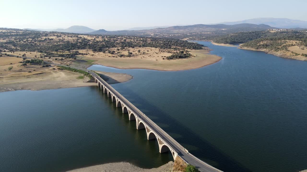 用无人机鸟瞰一个巨大的蓝色湖泊，有一座桥连接沼泽的海岸，萨拉曼卡，西班牙。视频素材