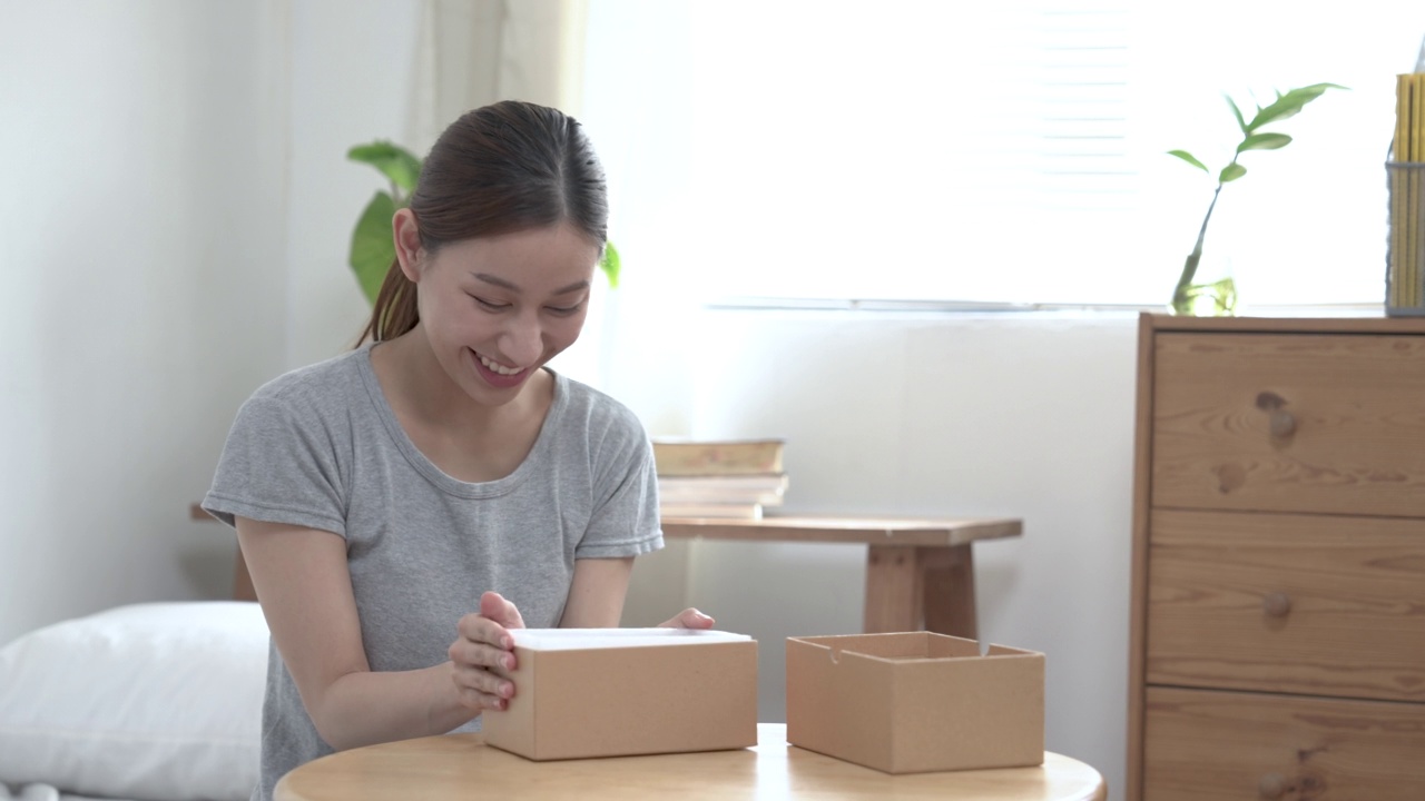 一名亚洲妇女兴奋地打开一个邮包，她看到了邮包里的东西，表现出高兴的表情。视频素材