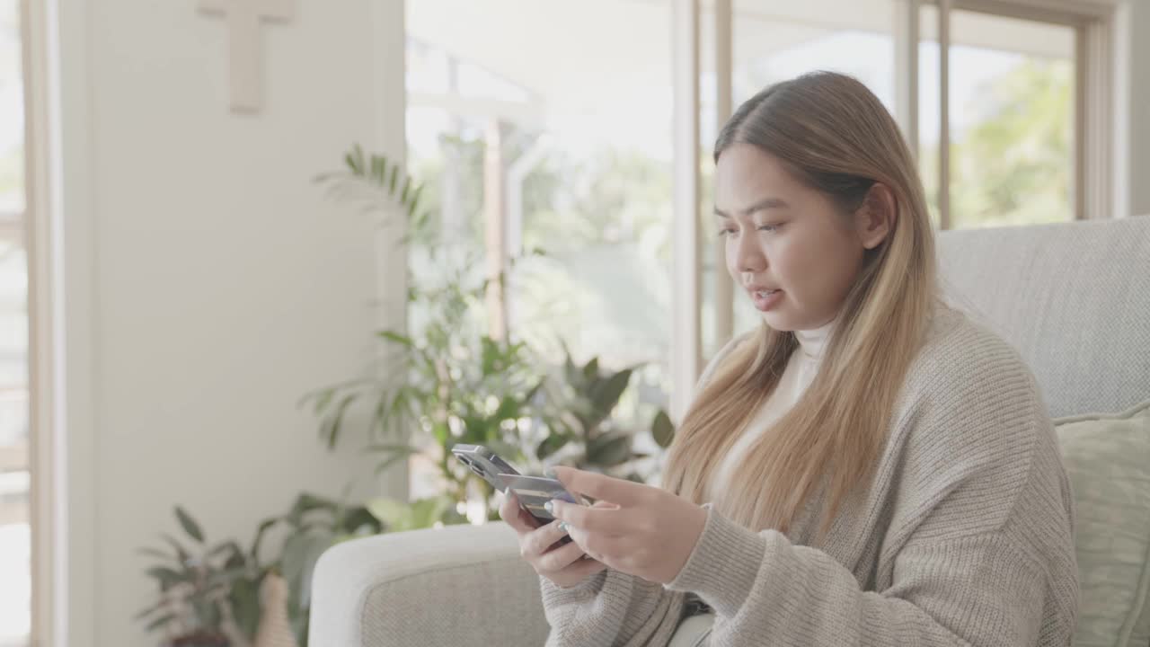 亚洲年轻成年女性在家里使用手机在线购物视频素材