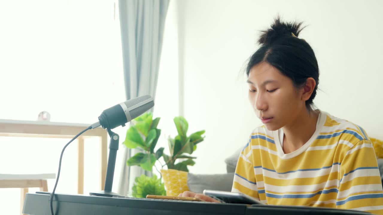 亚洲女孩在家靠窗的沙发上用手机app学习键盘乐器，生活理念。视频素材